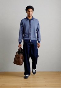 Μπλε σκούρο ζακέτα με υφή και γιακά σε αντίθετο χρώμα, σε συνδυασμό με άνετο παντελόνι σκούρου χρώματος και καφέ δερμάτινη τσάντα. Καθημερινά αθλητικά παπούτσια.