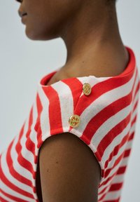 Top de punto a rayas rojas y blancas con escote barco, mangas cortas y dos botones decorativos dorados en los hombros.