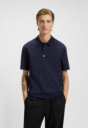 Marineblaues Poloshirt mit kurzen Ärmeln und Kragen, das ein kleines Logo auf der Brust trägt. Der Stoff wirkt glatt und leicht strukturiert.