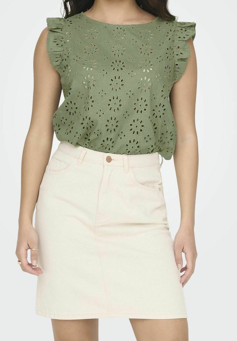 Blusa di cotone verde con ritagli floreali e maniche a volant, abbinata a una gonna di jeans rosa chiaro con tasche frontali e chiusura a bottone.
