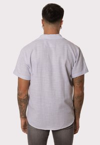 Camisa de manga corta gris claro, de tela texturizada, con cuello abotonado, dobladillo curvado; la vista trasera muestra detalles de costura y sin marca visible.