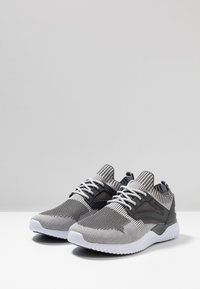 Zapatillas deportivas gris y blancas con un upper de tejido texturizado, acentos negros contrastantes y una suela de goma blanca. Incluye cordones tradicionales.