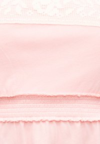 Ροζ ύφασμα με στρωματοποιημένες υφές, που περιλαμβάνουν καμπύλη ζώνη με ραβδώσεις και λεπτομέρεια δαντέλας στην επάνω άκρη.