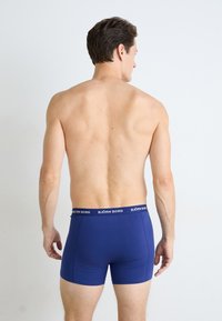 Mann som står med ryggen til kameraet og har på seg blå Björn Borg boxershorts mot en enkel hvit bakgrunn.