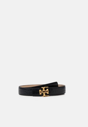 Czarny teksturowany skórzany pasek z ozdobną złotą klamrą o symetrycznym wzorze wycięć, położony płasko na jednolitym jasnym tle.