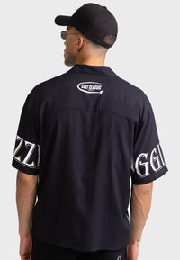 Μαύρο κοντομάνικο μπλουζάκι με λευκό κείμενο στα μανίκια και στην πλάτη, με άνετη εφαρμογή και ομαλή υφή υφάσματος.