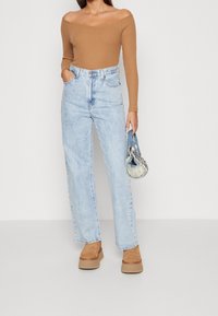 Light blue high-waisted jeans with a relaxed fit, paired with a brown off-the-shoulder top and beige platform shoes, holding a small textured bag.