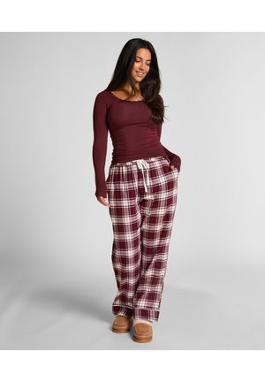 Haut à manches longues bordeaux associé à un pantalon à carreaux bourgogne et blanc, avec taille élastique et poches latérales. Des pantoufles beige complètent la tenue.