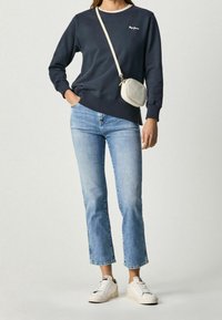 Granatowy sweatshirt z prążkowanymi mankietami, jasnoniebieskie dżinsy z krótkim nogawkiem oraz białe trampki; uzupełnione o małą torebkę na ramię.