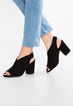 Sandales à talons ouverts en suède noir avec un design découpé et une bride à la cheville. Talon block pour plus de stabilité. Fini texturé qui améliore l'apparence générale.