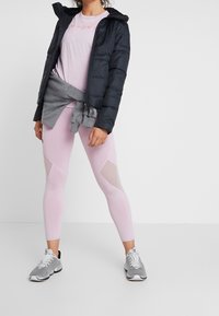 Czarna kurtka puchowa, jasnoróżowy t-shirt, szary sweter związany w talii, różowe leginsy z siateczkowymi akcentami oraz szare trampki.