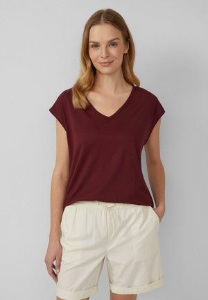 T-shirt bordeaux a V in tessuto morbido, con maniche corte e vestibilità rilassata, abbinata a pantaloni corti beige chiaro con vita elastica.