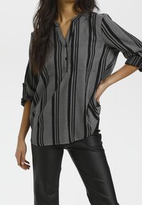 Zwart-wit gestreepte blouse met knoopsluiting, ontspannen pasvorm, opgerolde mouwen en een textuurstof, gecombineerd met zwarte rok van kunstleer.