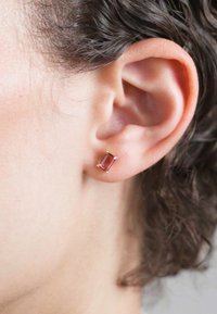 Rozā dārgakmens auskari, kas izgatavoti no zelta nokrāsas metāla. Auskari ir taisnstūra formas, ar četriem stiprinājumiem, kas notur dārgakmeni.