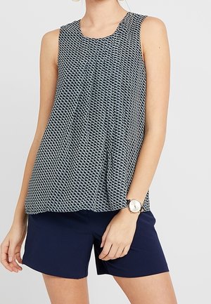 Mouwloze blouse in een marineblauwe en witte patroonstof, met plooien en een ronde halslijn, gecombineerd met marineblauwe short en een polshorloge.
