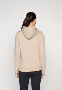 Haut à capuche beige avec cordon de serrage, fabriqué en tissu doux. Comprend des manches longues et une taille ajustée, associé à un legging noir.