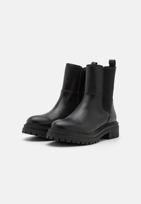 Botas de tobillo de cuero negro con paneles laterales elásticos, punta redonda, suela de goma negra gruesa y tirador en la parte posterior para facilitar su uso.