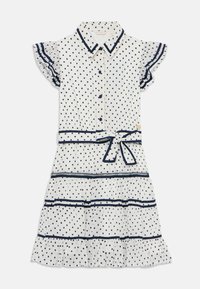 Robe blanche à pois navy. Manches courtes à volants, devant à boutons et taille nouée. Présente des volants superposés au bas et un passepoil contrastant.