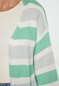 Lehký cardigan s alternativními pruhy v mátově zelené, šedé a bílé barvě. Vyroben z pletené látky s volným, otevřeným designem.