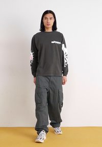 Dark gray long-sleeve shirt with white graphic designs on sleeves, paired with loose-fitting cargo pants and white athletic shoes.