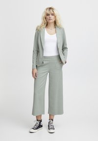 Lichtgroen geruit pak met een op maat gemaakte blazer en wijde broekspijpen, gecombineerd met een witte tanktop en zwarte hoge sneakers.