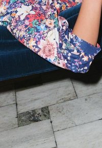 Blumenmusterstoff mit lebhaften Farben, der große Blumen auf einem dunkelblauen Hintergrund zeigt. Weiches, strukturiertes Material neben einem blauen Samtsofa.