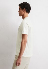 Light-colored, short-sleeve cotton t-shirt with a crew neck; features simple printed design on the front; worn with light-colored pants.