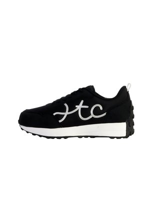Zwarte sneaker met een bovenwerk van suede, zilveren logo omlijnd aan de zijkant, en witte tussenzool; heeft een gestructureerde zwarte rubberen buitenzool.