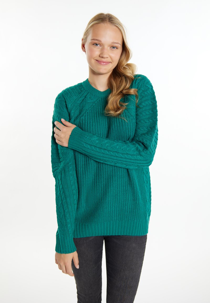 Maglione teal lavorato a maglia con motivi a cavo testurizzati, collo rotondo e maniche lunghe. Abbinato a jeans scuri. Finitura del tessuto liscia.