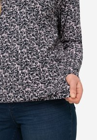 Camicia a maniche lunghe con sfondo blu navy e motivo astratto rosa. Tessuto morbido con vestibilità rilassata, orlo che si trova appena sopra la vita.