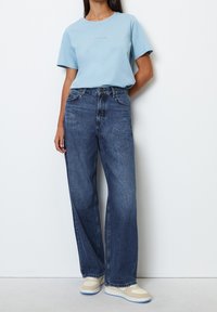 Light blue cotton T-shirt with short sleeves and crew neck, paired with high-waisted, wide-leg dark blue jeans and beige sneakers.