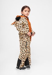 Lodjurstrykt snowsuit i beige och orange, med en huva med pälsdetaljer, svarta accenter och dragkedjefickor; vattentätt material.