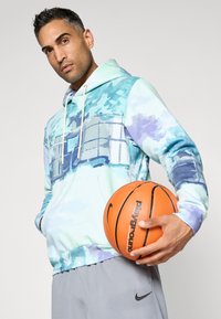 Felpa con cappuccio in un motivo astratto blu chiaro e verde, con una tasca frontale e lacci bianchi, abbinata a pantaloni corti sportivi grigi e a un pallone da basket.