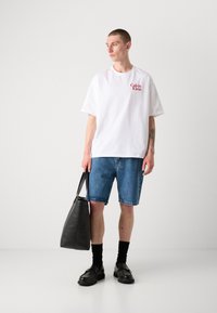 Balta trumpa rankovėmis marškinėliai su raudonu Calvin Klein logotipu, derinami su mėlynomis džinsinėmis šortais. Juoda odinė rankinė, juodos kojinės ir batai.
