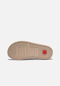 Beige rubberen zool met een gestructureerd oppervlak, een reliëflogo "fitflop," en een ronde rode accent bij de hiel voor extra grip.