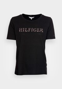 Camiseta negra de manga corta hecha de algodón, con un logo "HILFIGER" centrado en el pecho en color rosa. Cuello redondo, corte relajado.