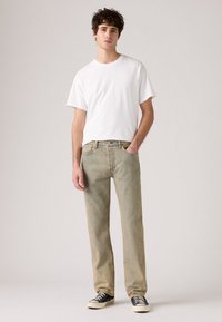 Jeans de mezclilla verde claro con un corte recto, combinados con una camiseta blanca lisa y zapatillas bajas negras con suelas blancas.