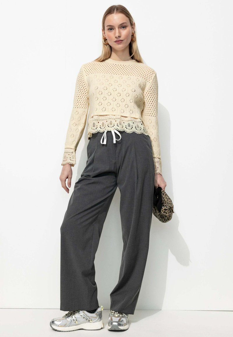 Haut en tricot crème avec un motif en maille, ourlet en dentelle, associé à un pantalon large gris et des baskets argentées. Accessoire : petit sac à main en imprimé léopard.