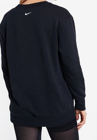 Sweatshirt noir à col rond, manches longues et poignets côtelés. Presentant un petit logo Nike blanc au haut du dos. Texture de tissu douce.