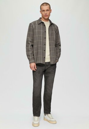 Veste à carreaux grise avec des boutons noirs, portée sur un pull crème et associée à un jean foncé et des baskets blanches.