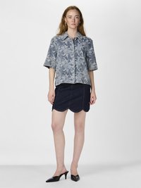 Denimskjorta med blommönster i ljusblått, korta ärmar och spetsig krage, kombinerad med en mörkbå blå kjol med scalloped nederkant och svarta slingback-klackar.