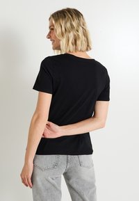 Camiseta negra de manga corta hecha de algodón, con escote redondo y un diseño ajustado, combinada con unos vaqueros de tiro alto en gris claro.