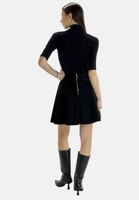 Zwarte top met korte mouwen gecombineerd met een zwarte flared rok met een ritssluiting aan de achterkant. Het model draagt kniehoog, glanzende zwarte hakken.
