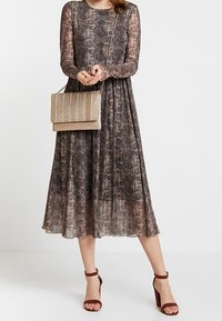 Sukienka z długim rękawem w stonowanych kolorach z wzorem i zwiewną spódnicą. Posiada okrągły dekolt oraz delikatną koronkową teksturę. Dopełniona złotą torebką.