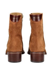 Braune Wildleder-Stiefeletten mit einem leichtem Absatz, ausgestattet mit einem glatten Leder-Oberkante, goldenen Hardware-Reißverschluss und geprägtem Logo auf der Rückseite.
