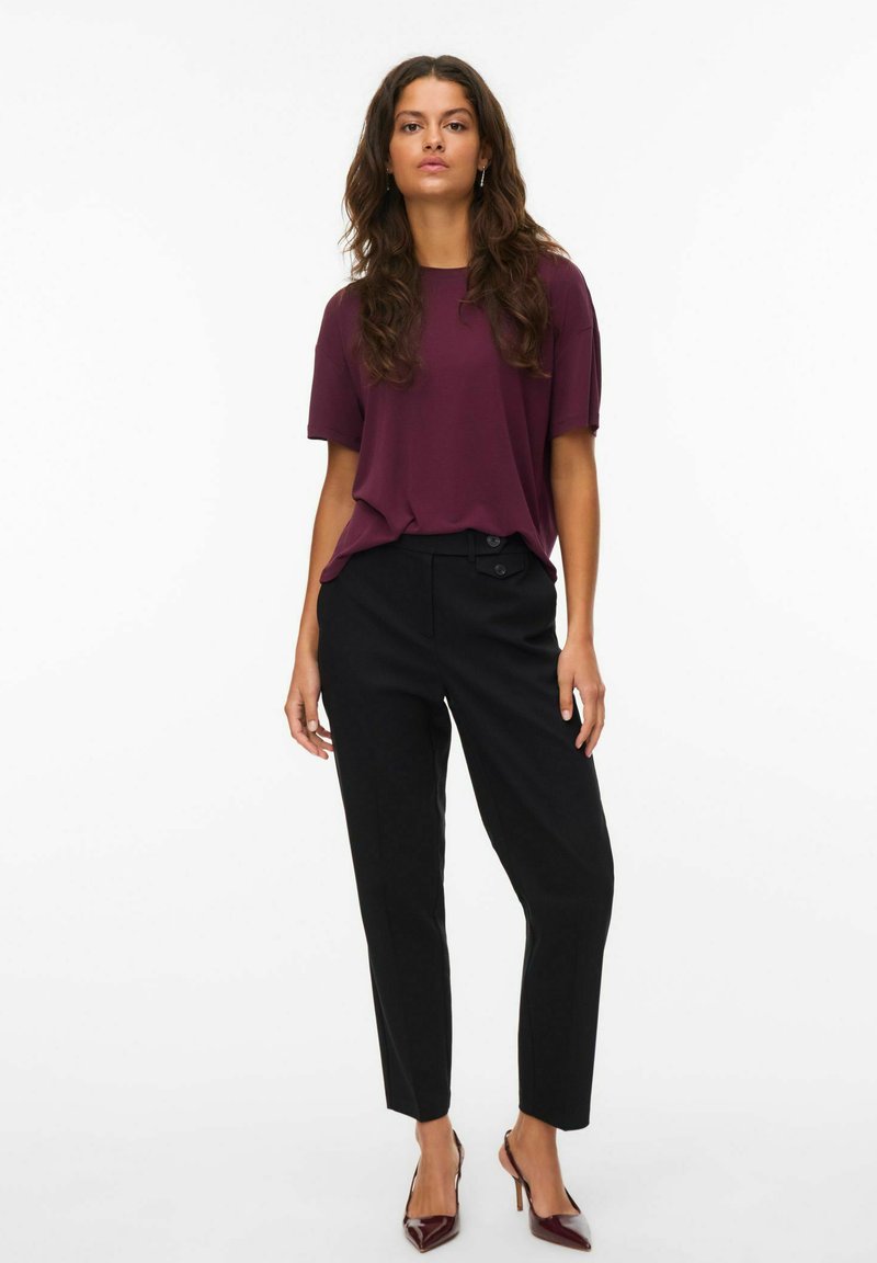 Burgundyröd kortärmad topp i kombination med svarta skräddarsydda byxor och mörk burgundyröda klackar. Outfiten har en avslappnad passform och slät tyg.