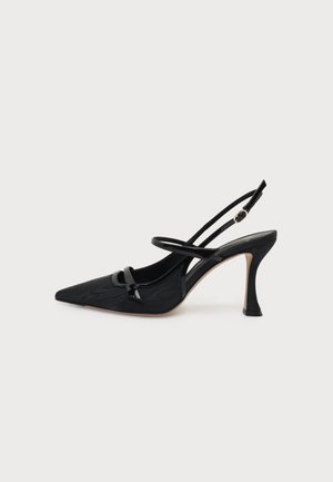 Μαύρο ψηλοτάκουνο slingback με μυτερή μύτη, λεπτά λουράκια στον αστράγαλο και στην καμάρα, πλαϊνή αγκράφα και καμπυλωτό τακούνι στιλέτο σε ανοιχτό φόντο.