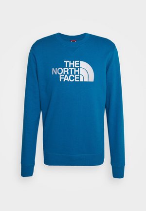 Blå sweatshirt med rund hals, lange ærmer og ribbet manchet. Har en stor, hvid logo tekst "THE NORTH FACE" på forsiden.