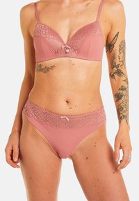 Ensemble de lingerie rose comprenant un soutien-gorge rembourré avec des détails en dentelle et une culotte assortie. Les deux pièces affichent un motif géométrique et un accent en forme de nœud.