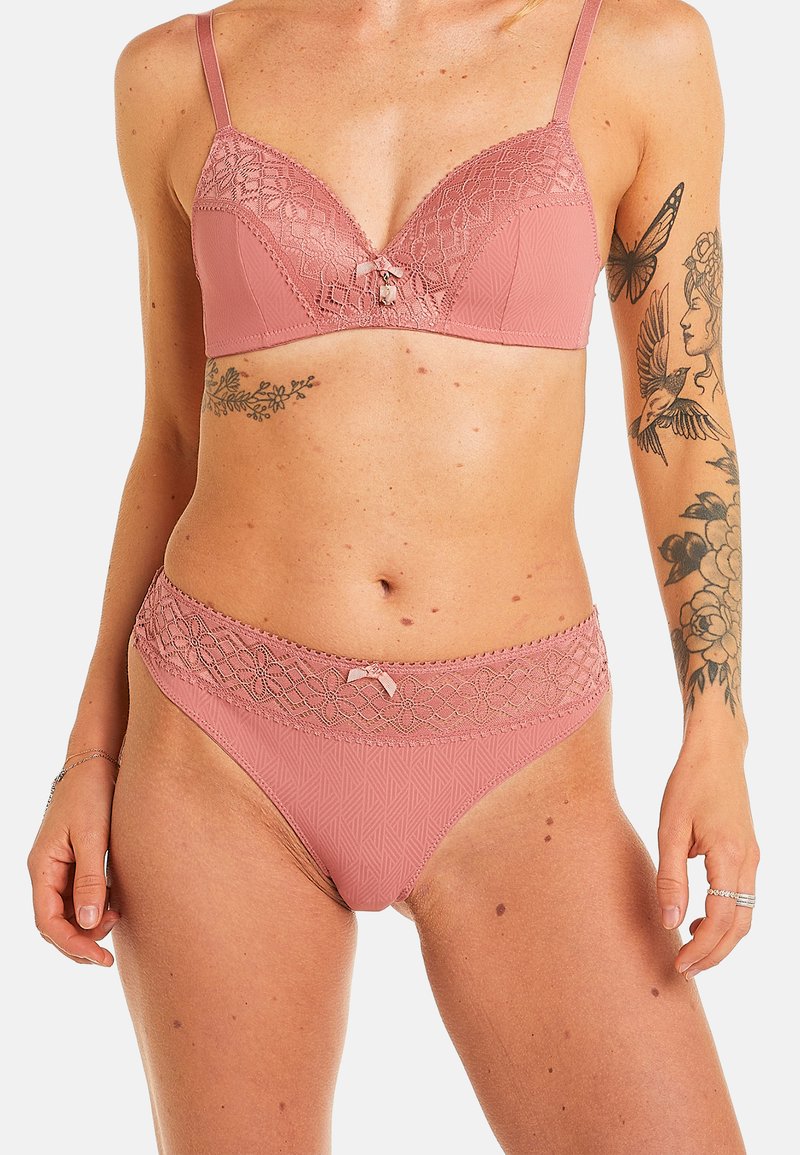 Ensemble de lingerie rose comprenant un soutien-gorge rembourré avec des détails en dentelle et une culotte assortie. Les deux pièces affichent un motif géométrique et un accent en forme de nœud.